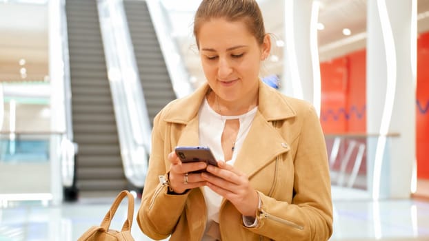 Portrait of young smiling woman using smartphone in big shopping mall.