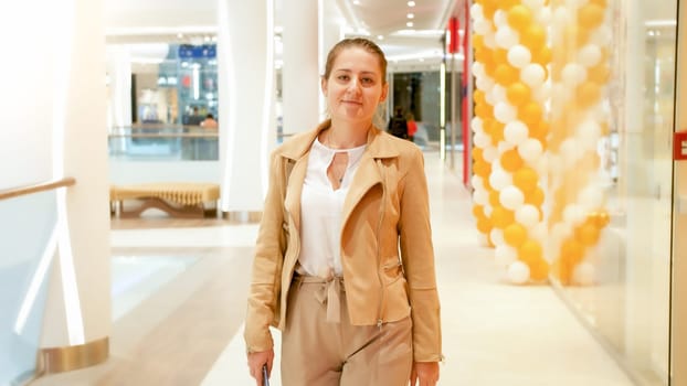 Portrait of beautiful smiling woman walking in long hallway at shopping mall.