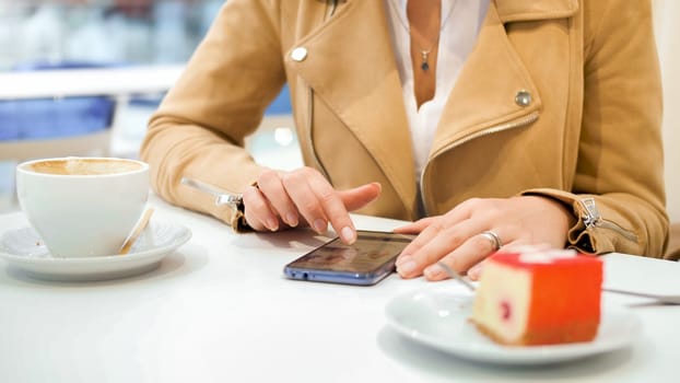 Closeup photo of young woman typing meassge in social media on smartphone while sitting in cafe.