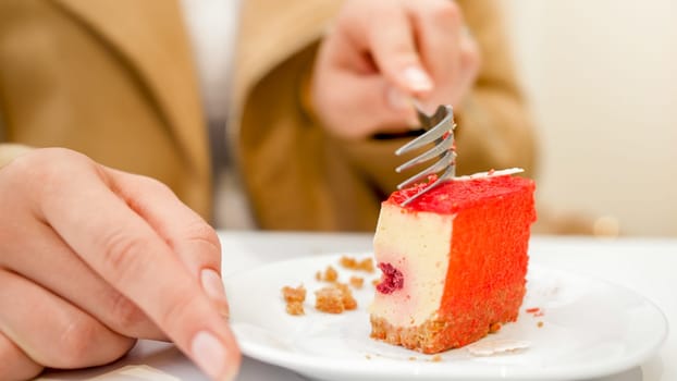 Closeup image of young woman holding fork and eating sweet red cake.