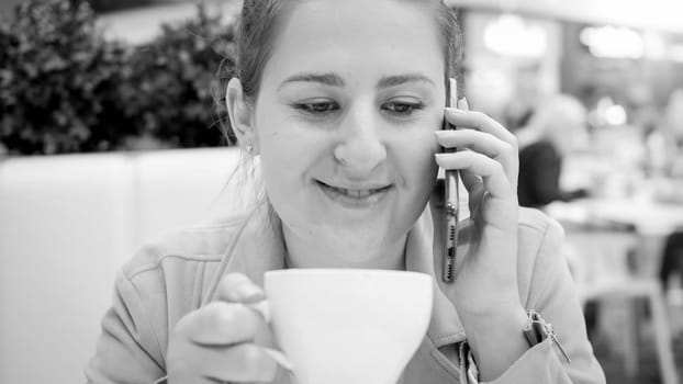 Black and white portrait of smilng young woman drinking coffee and talking by phone.