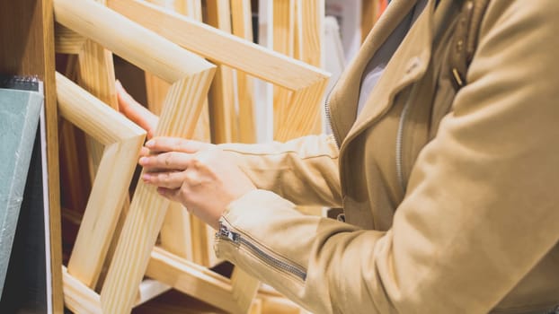 Closeup toned photo of female artist buying wooden frame for new painting in hobby store.