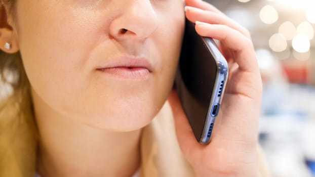 Closeup image of female mouth talkin by phone in cafe.