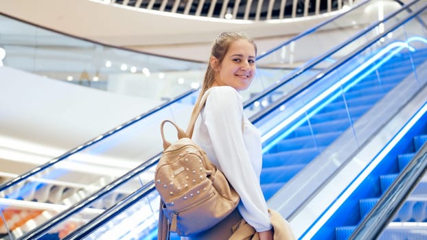Portrait of beautfiul smiling woman with bag standing on escalator in shopping mall.