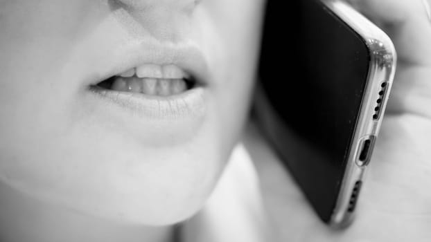 Black and white closeup photo of female mouth and lips talking by phone.