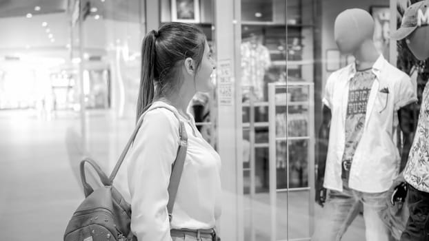 Black and white portrait of beautiful smiling woman choosing new clothes in shopping mall.