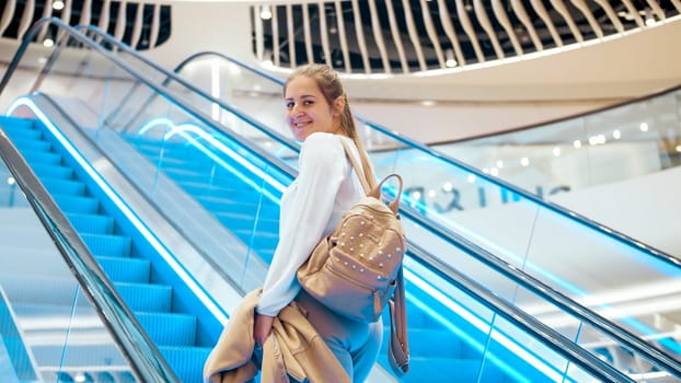 Portrait of beautiful smiling young woman going up on the escalator in shopping mall.