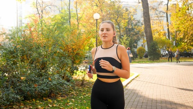 Portrait of beatiful young woman listening to music and running at autumn park.