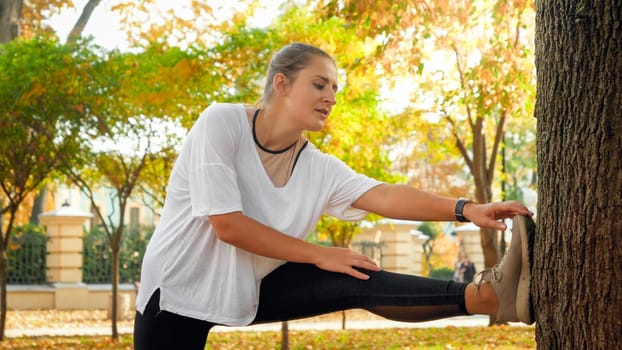 Portrait of sporty young woman stretching her muscles before doing sports exercises in autumn park.
