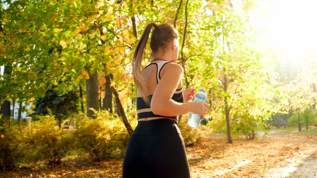 Beautiful sexy woman holding bottle of water while running in autumn park.