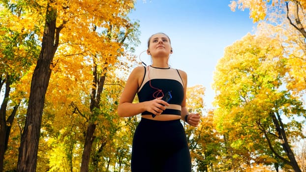 Portrait of beautiful smiling woman with earphones running at atumn park.