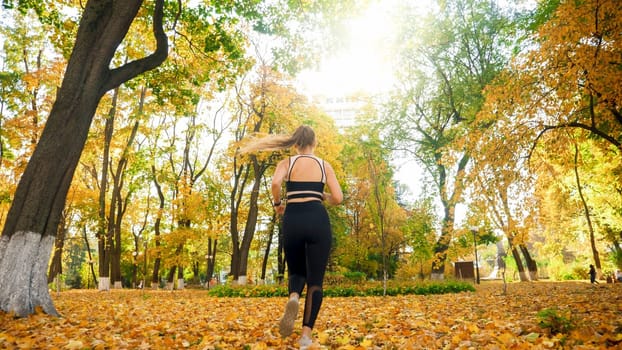 Rear view photo of sexy young woman in leggings running at autumn park.