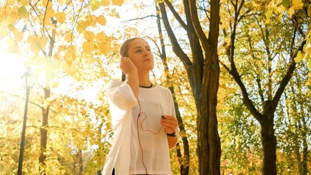 Portrait of beautiful young woman putting on headphones with music before jogging at autumn park.