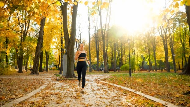 Beautiful young woman in leggings running on narrow path in autumn park.