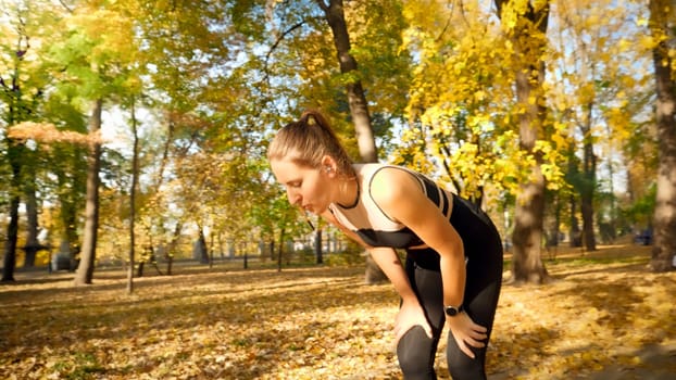 Prtrait of tired and exhausted young woman breathing and taking a break while jogging in autumn park.