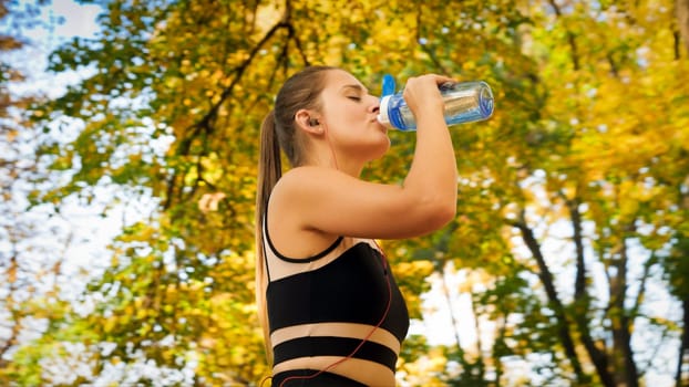 Portrai tof young woman listening music and drinking water while exercising in park.