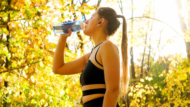 Sexy sporty woman with ponytail drinking water in autumn park.