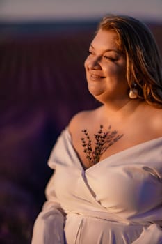 Woman poses in lavender field at sunset. Happy woman in white dress holds lavender bouquet. Aromatherapy concept, lavender oil, photo session in lavender.