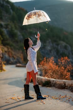woman umbrella leaves , She holds him over her head, autumn leaves are falling out of him. Beautiful woman in a dress with an umbrella in the autumn park on the road in the mountains