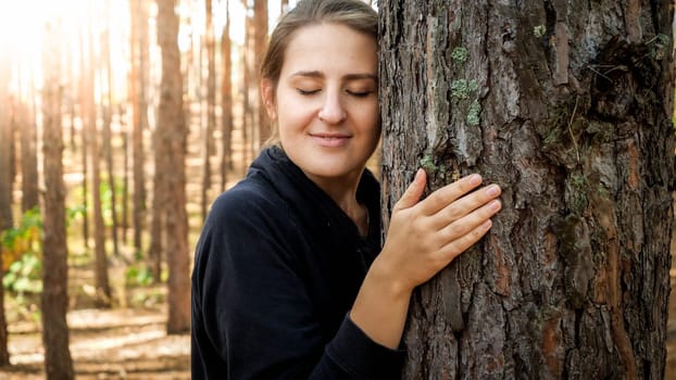 Portrait of beautiful young woman leaning and touching big old tree in forest. Concept of ecology, environment protection and harmony with nature.