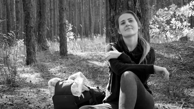 Black and white photo of smiling dreaming female tourist resting by the pine tree in forest.