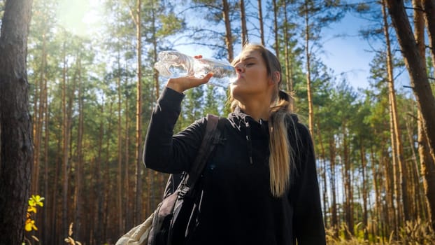 Cloesup portrait of beautiful hiking woman drinking water while travelling in pine forest.