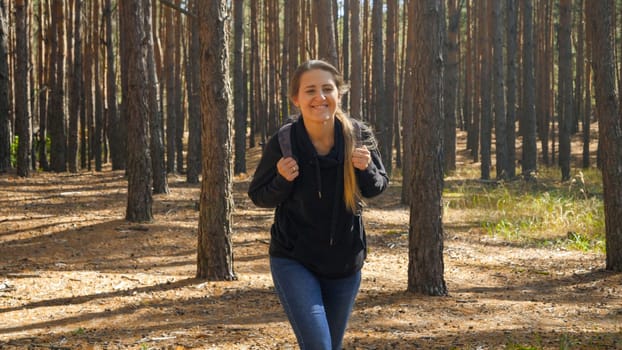 Toned portrait of happy smiling young woman with backpack hiking and walking in forest at autumn.