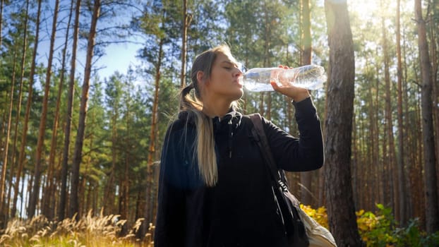 Portrait of beautiful female tourist having a break and drinking water from plastic bottle in forest.