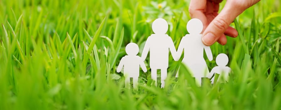 Figures of family of two parents and two children on green grass in sunny day. Conceptual symbol of people relationship.