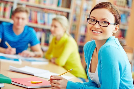 Female student sitting in college library and looking at camera