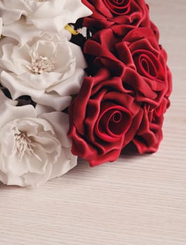 artificial bouquet of red and white roses on wooden surface with space for text