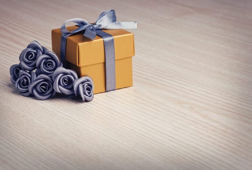 grey flowers and golden gift box with ribbon on wooden surface with space for text