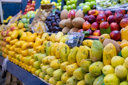 Colorful fruit stand with fresh mangoes, mamey, peaches, green apples, and more. Juicy-looking fruit for sale on stall inside classic Mexican market. Healthy food