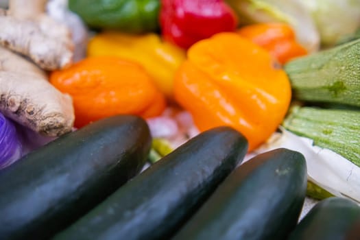 Close-up of orange, green, and red bell peppers, cucumbers, zucchini, and ginger roots. Colorful and fresh-looking vegetables for sale. Natural healthy food