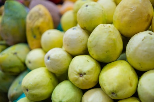 Close-up of colorful fruit stand with pile of fresh yellow guavas and mangoes. Juicy-looking tropical fruit for sale on stall inside classic Mexican market. Natural healthy food