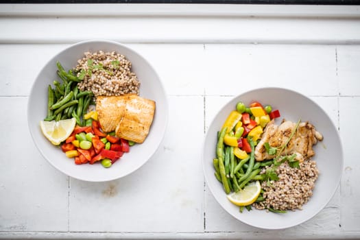 Top view of chicken and salmon dishes with buckwheat, green beans, broad beans, tomato, and pepper slices. Nutritious dishes with vegetables and meat on white plates. Healthy balanced diet
