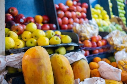 Colorful fruit stand with fresh papayas, yellow and red apples, tangerines, and more. Juicy-looking fruit for sale on stall inside classic Mexican market. Healthy food