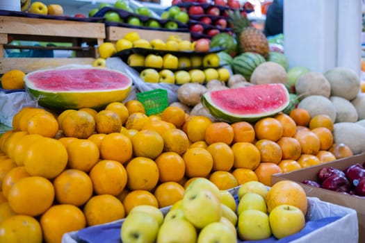 Colorful fruit stand with fresh oranges, sliced watermelons, yellow apples, melons, and more. Juicy-looking fruit for sale on stall inside classic Mexican market. Healthy food