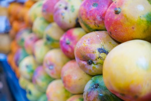 Close-up of colorful fruit stand with pile of fresh keitt mangoes, tangerines, and more. Close-up of juicy fruit for sale on stall in classic Mexican market. Healthy food