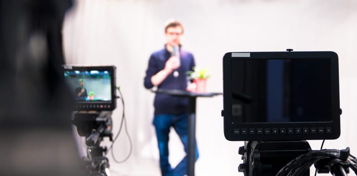 Male journalist in a television studio talks into a microphone, film cameras