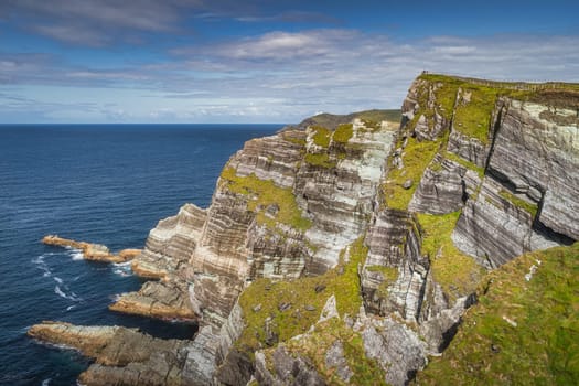 Tourists standing on the top of majestic and beautiful Kerry Cliffs with a view on Atlantic Ocean, sunny summer day, Portmagee, Ring of Kerry, Ireland