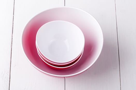 An empty red Salad Bowl and three cups on a white wooden table