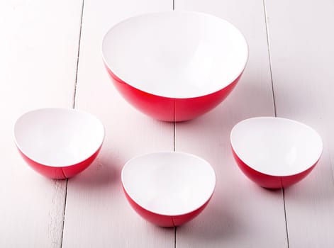 An empty red Salad Bowl and three cups on a white wooden table
