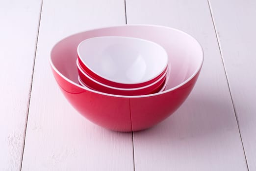 An empty red Salad Bowl and cups on a white wooden table
