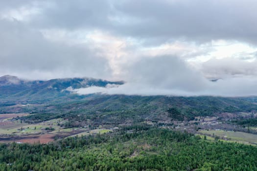Beautiful and peaceful forest under cloudy sky and with mountains as background. Aerial view of cloudy and foggy skyline above the woods. Wooded and rocky landscapes