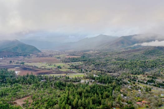 Beautiful and peaceful forest under cloudy sky and with mountains as background. Aerial view of cloudy and foggy skyline above the woods. Wooded and rocky landscapes