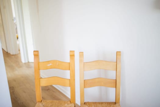 Two wooden chairs on long empty hall with white walls and wooden floor. Brown hairs inside house with white interiors. Minimalistic design furniture