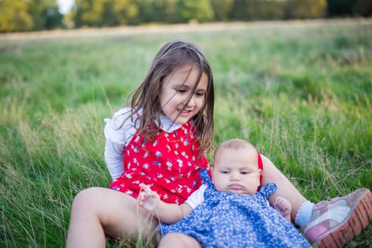 Happy and adorable little girl and baby lying down on grass. Portrait of cute young child sitting next to her baby sibling in park. Young family playing outdoors