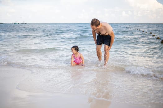 Happy father and young daughter joyfully playing in the water at the beach. Man and cute young child having fun in sea. Tropical summer vacations