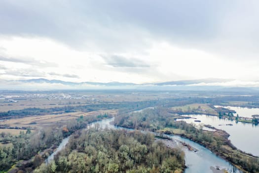 Peaceful rivers surrounding the forest with mountains far in the distance. Beautiful aerial view of rivers going through the woods under cloudy sky. Wooded and rocky landscapes